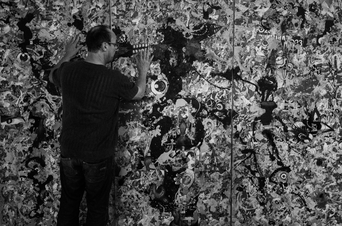 Jacques Verdier, de dos, les mains posées sur l'une de ses toiles